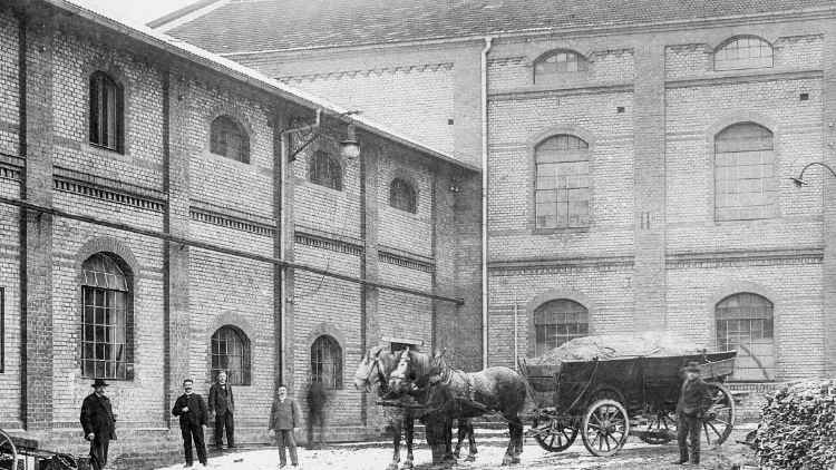 Historisches Foto: Arbeiter und ein Pferdefuhrwerk vor dem Backsteingebäude der Brennerei